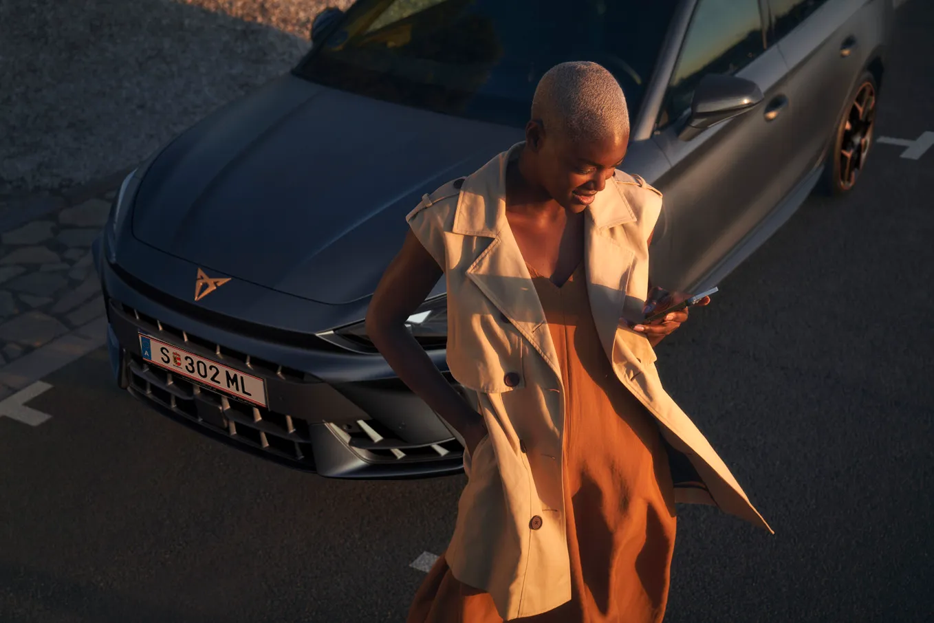 Frau sieht auf das Handy vor dem CUPRA Modell.
