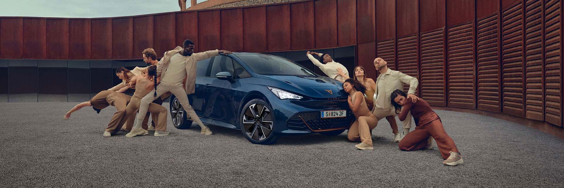Ein blauer CUPRA Born steht auf einem Platz, mehrere Personen befinden sich links und rechts neben dem Fahrzeug.