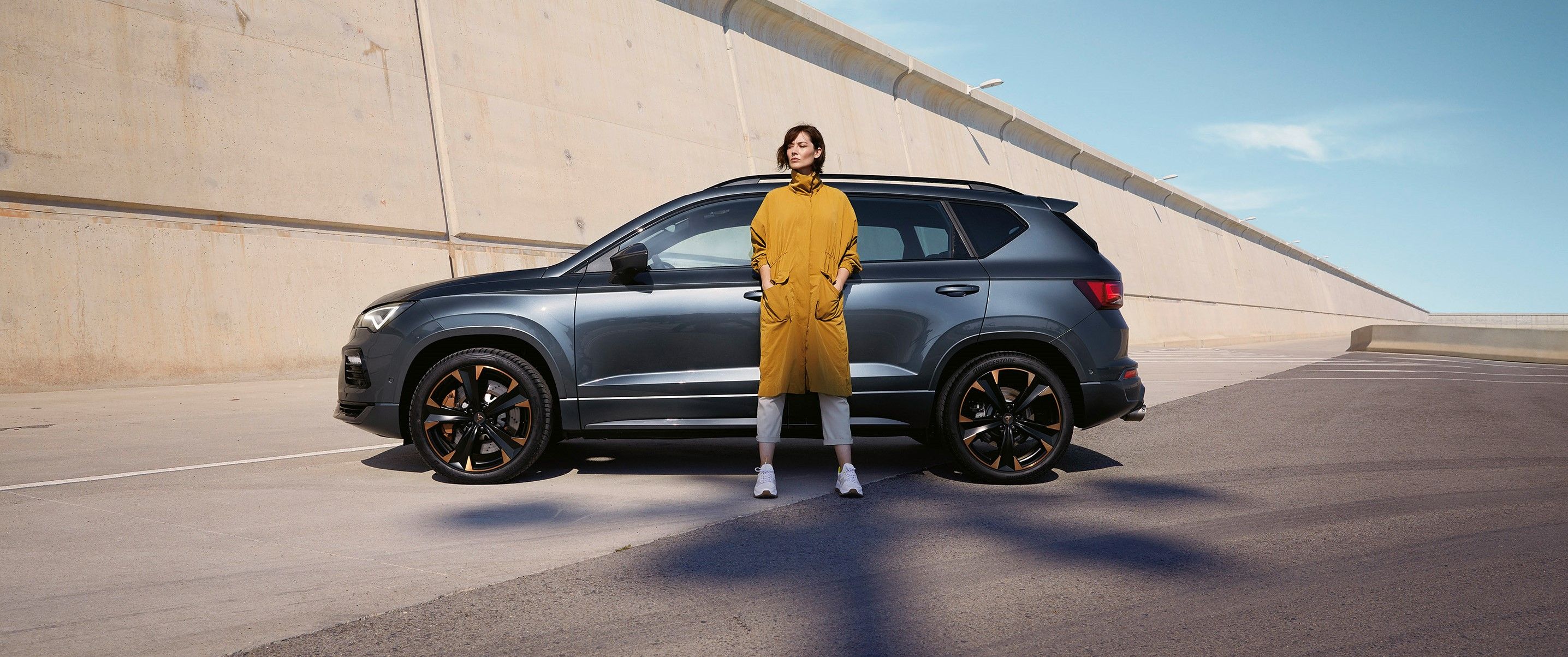 Ein CUPRA Ateca in grau, eine Frau steht davor.