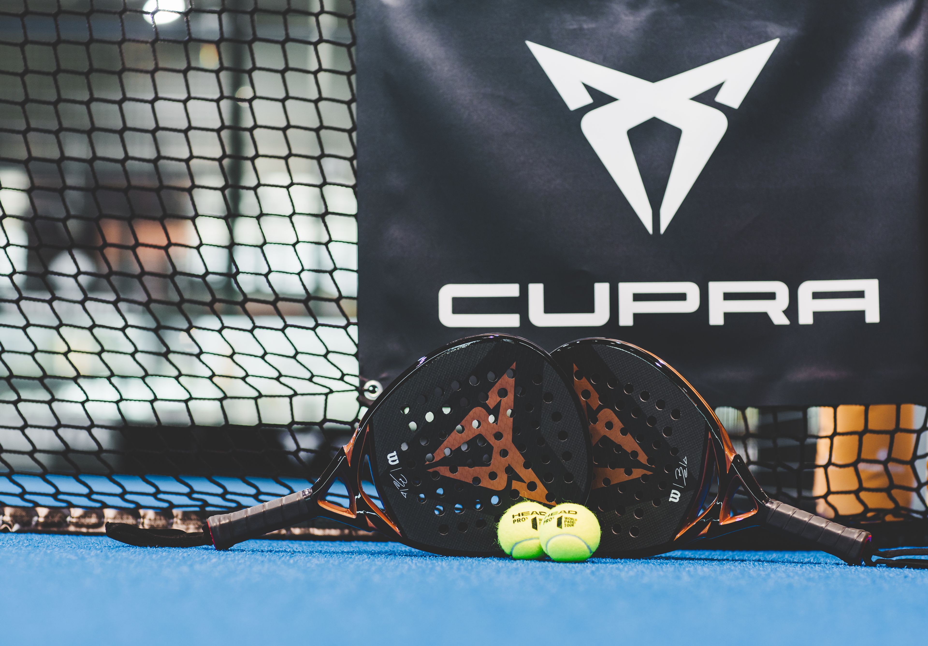 Zwei CUPRA Padels und zwei Bälle vor einem CUPRA Logo.