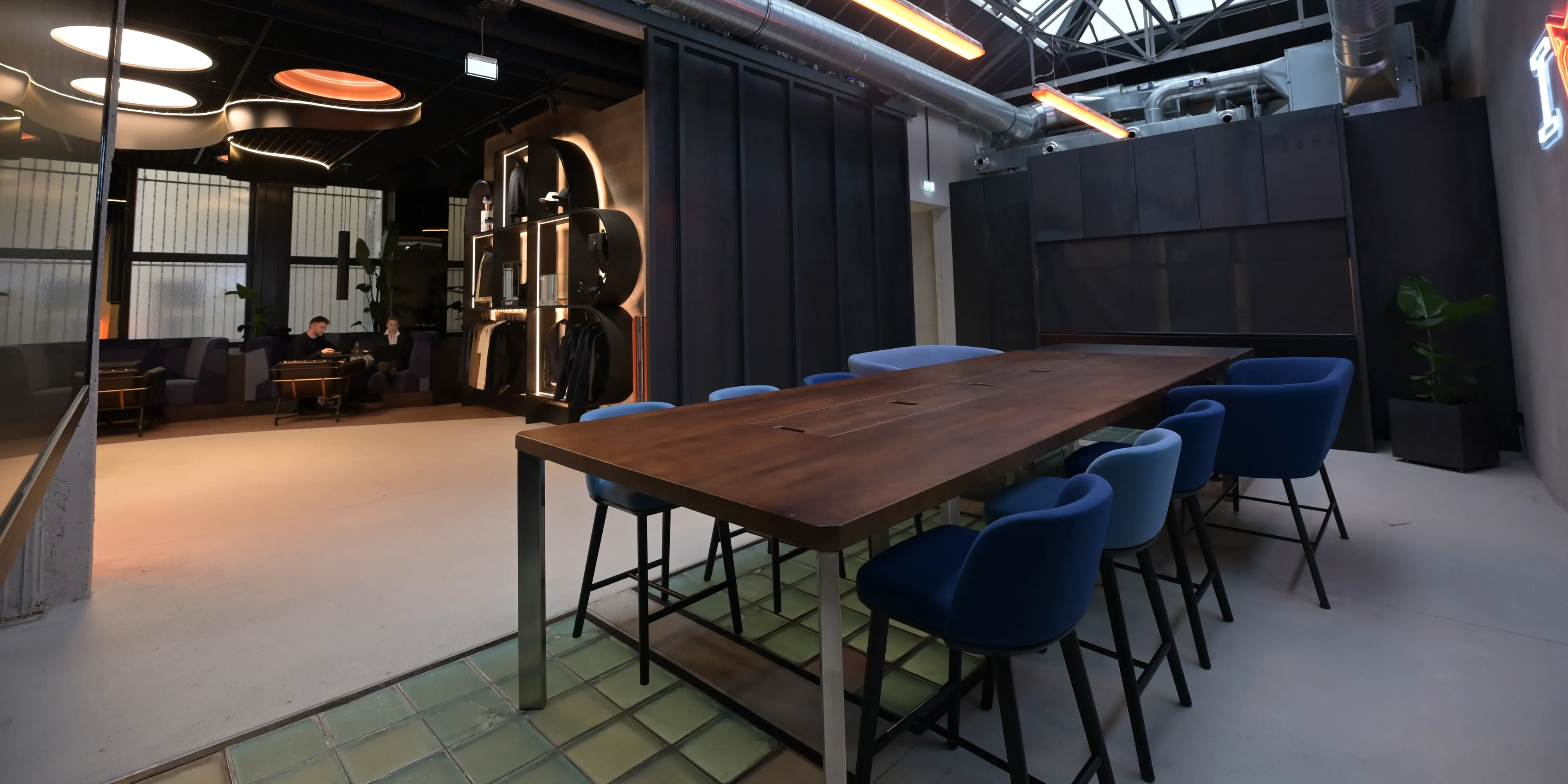 Konferenzraum mit langem Bartisch, passenden Barhockern und integrierter Küchenzeile sowie Blick auf die Businesslounge 